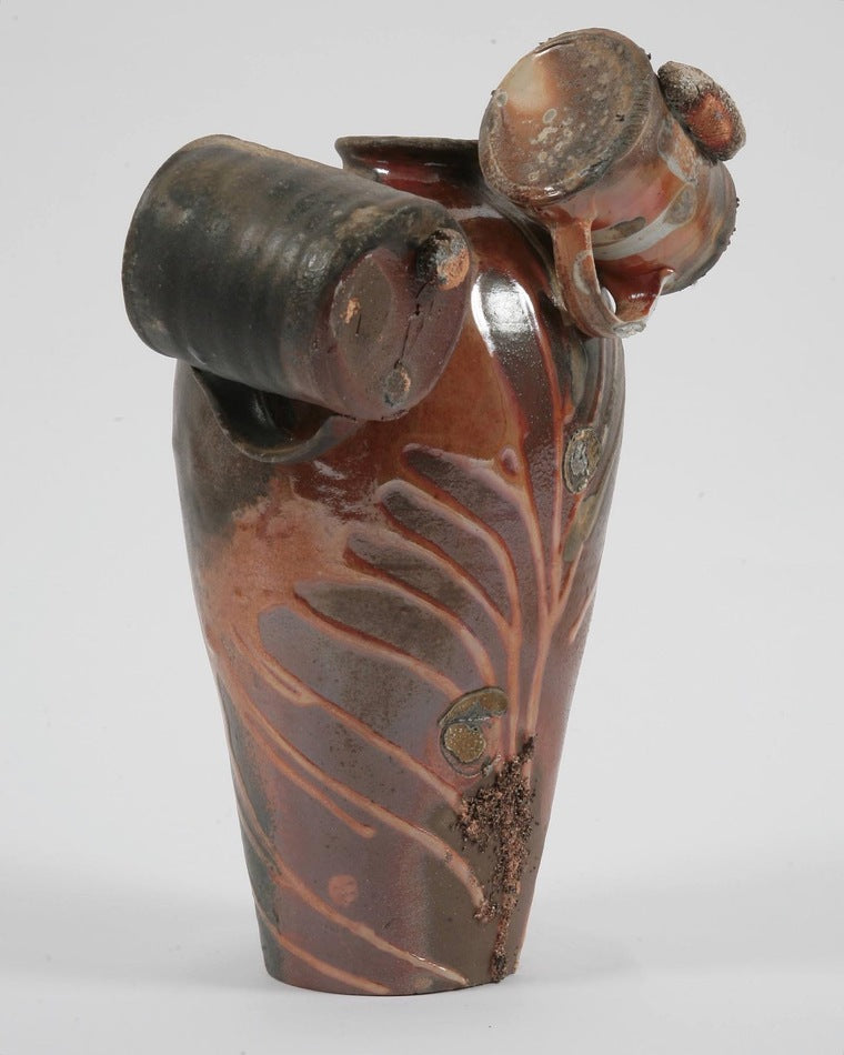 A long wheel thrown ceramic vase with two mugs melted on at the very top