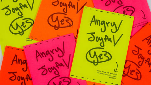 Scattered collection of brightly coloured neon booklets reading "Angry/Joyful/Yes: Some ways of working through marginalised emotion" in handwriting