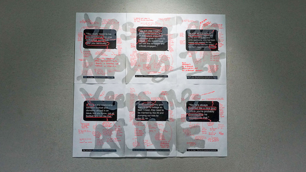 Six posters with black speech bubbles and pink handwritten text pinned next to each other in two rows. Silver spray paint letters reading "Yes, I am angry. It keeps me alive" stretch across all the posters. 
