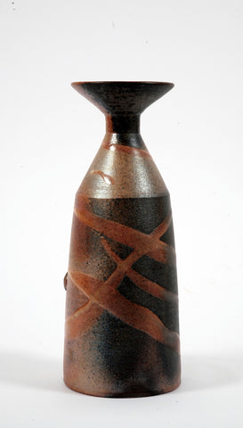 A narrow bottle with a flared angular neck, the piece is a mottle orange with slashes of white glaze across it 