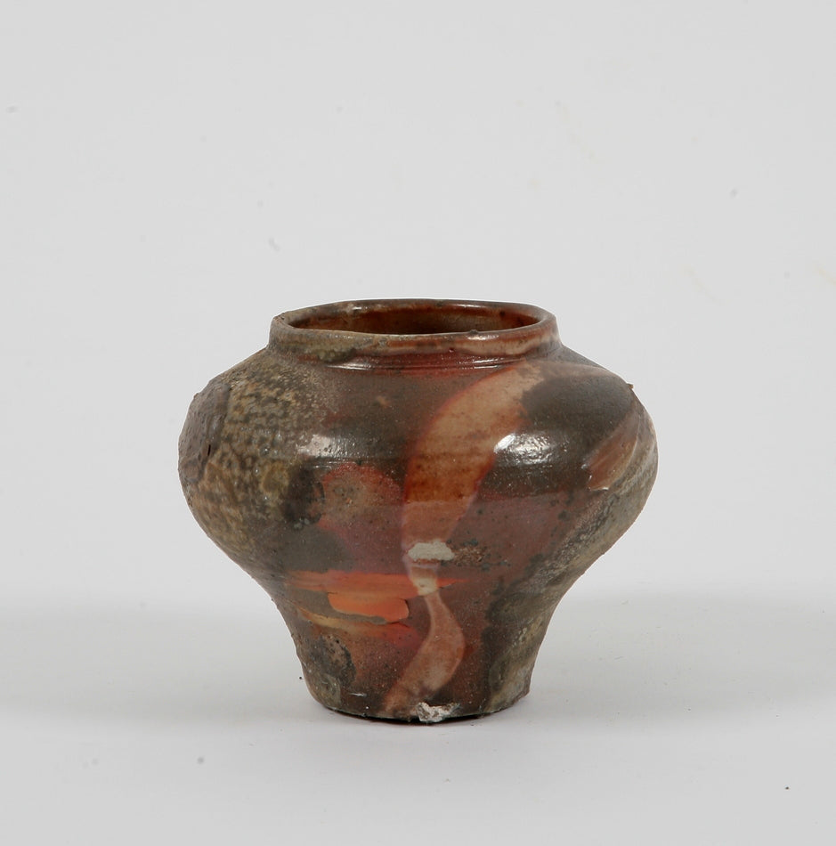 A small ceramic vessel with a narrow base and a rounded upper half with an open rim 