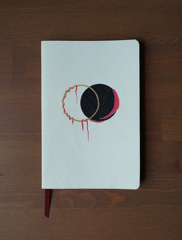 An ivory coloured  notebook with a design on the cover. Ven Diagram in black, red and gold with vines hanging from it. 